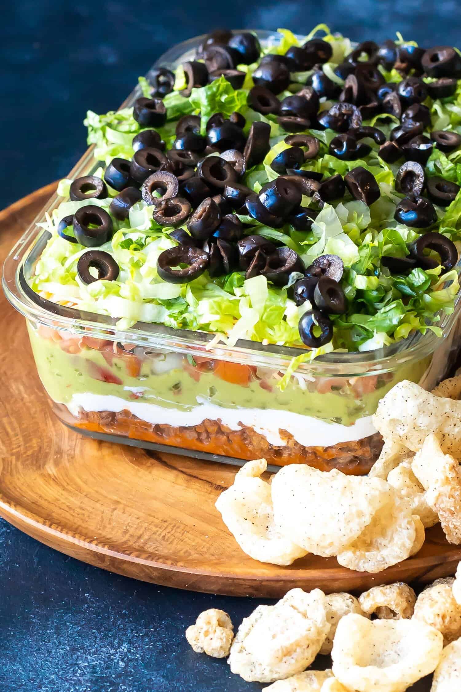 Keto 7 Layer Taco Dip in glass bowl showing the layers with pork rinds scattered around